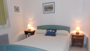 Een slaapkamer met een bed, twee nachtkastjes met lampen, een hoofdeinde, een ingelijst schilderij aan de muur en een raam met gordijn.