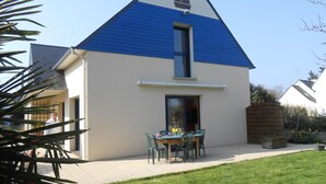 Een huis met een blauw dak, een klein balkon en een tafel met stoelen buiten.
