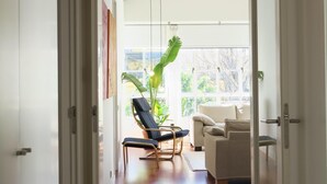 A hallway with a modern pendant light, a plant, and a view of a balcony with a chair and a sofa. - Amazing Apartment in Regionalist building (Sevilla)