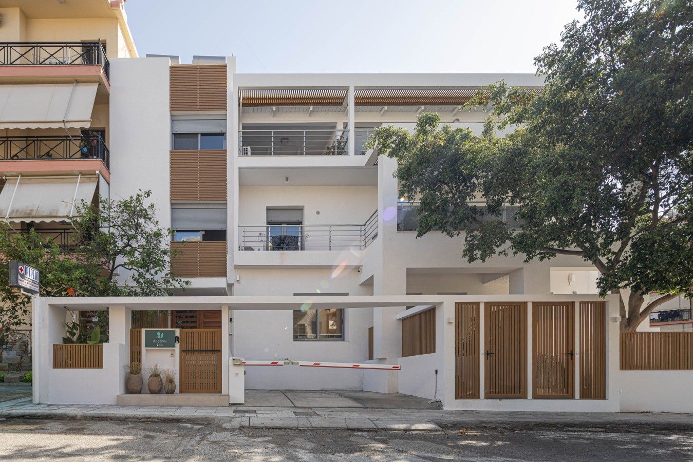 Un edificio residencial de varios pisos con entrada protegida, balcones y un jardín visible.