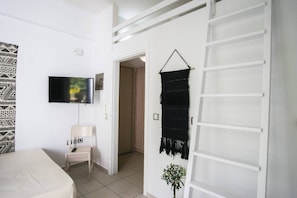A room with a bed, a TV mounted on the wall, a door with a macrame curtain, and a small plant.