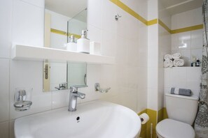Een badkamer met een wit wastafelmeubel, spiegel en toilet. Handdoeken en toiletartikelen hangen aan de muur.