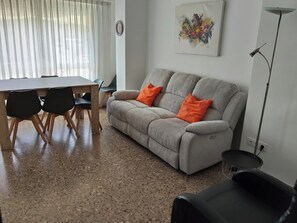 Una sala de estar con un sofá, dos almohadas naranjas, una mesa de comedor con sillas y un cuadro en la pared.