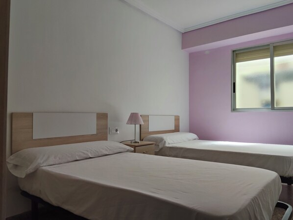 Habitación de hotel con dos camas, una mesita de noche con lámpara y una ventana con persianas.
