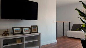 A modern living room with a flat-screen TV mounted on the wall, a white console table with framed pictures, and a large potted plant.
