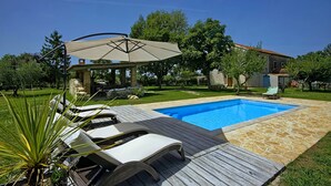 A backyard with a swimming pool, lounge chairs, and a pergola with an umbrella.