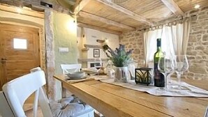A rustic dining area with a wooden table, white chairs, and a stone wall backdrop.