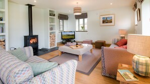 A cozy living room with a fireplace, comfortable seating, a television, and a bookshelf. -  DIGNITY - Beautiful Barn Conversion in Idyllic Countryside with Hot Tub (Galashiels)