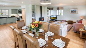 A dining area with a wooden table set for six, surrounded by leather chairs. A large vase with flowers is on the table, and a television is in the background. -  DIGNITY - Beautiful Barn Conversion in Idyllic Countryside with Hot Tub (Galashiels)