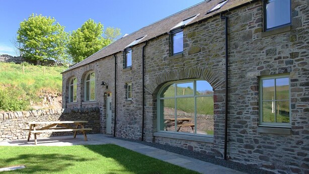 A stone building with arched windows and a picnic table in the foreground. -  DIGNITY - Beautiful Barn Conversion in Idyllic Countryside with Hot Tub (Galashiels)