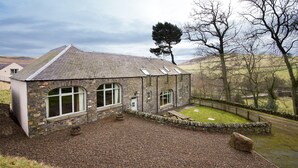 A stone building with arched windows and a sloped roof, surrounded by a stone wall and a grassy lawn. -  DIGNITY - Beautiful Barn Conversion in Idyllic Countryside with Hot Tub (Galashiels)
