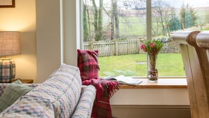 A cozy room with a large window, a sofa, a lamp, and a vase with flowers on the windowsill. -  DIGNITY - Beautiful Barn Conversion in Idyllic Countryside with Hot Tub (Galashiels)