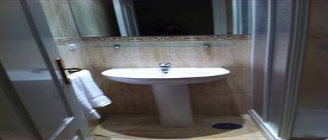A bathroom with a pedestal sink, a towel hanging on the door, and a mirror above the sink.