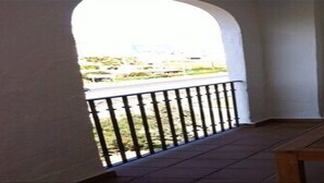 A balcony with a wooden table and chairs, a view of the street, and a door to the right. - Residencial Marina Duquesa 642 (Manilva)