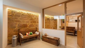 A cozy room with a stone wall, a wooden bench, a metal trash can, and a mirror reflecting another room.
