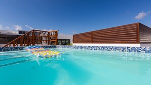 A swimming pool with a colorful inflatable float, a wooden deck structure, and a modern building with horizontal slats. - Central Amazing PH with Private Rooftop and Jacuzzi (Playa del Carmen)