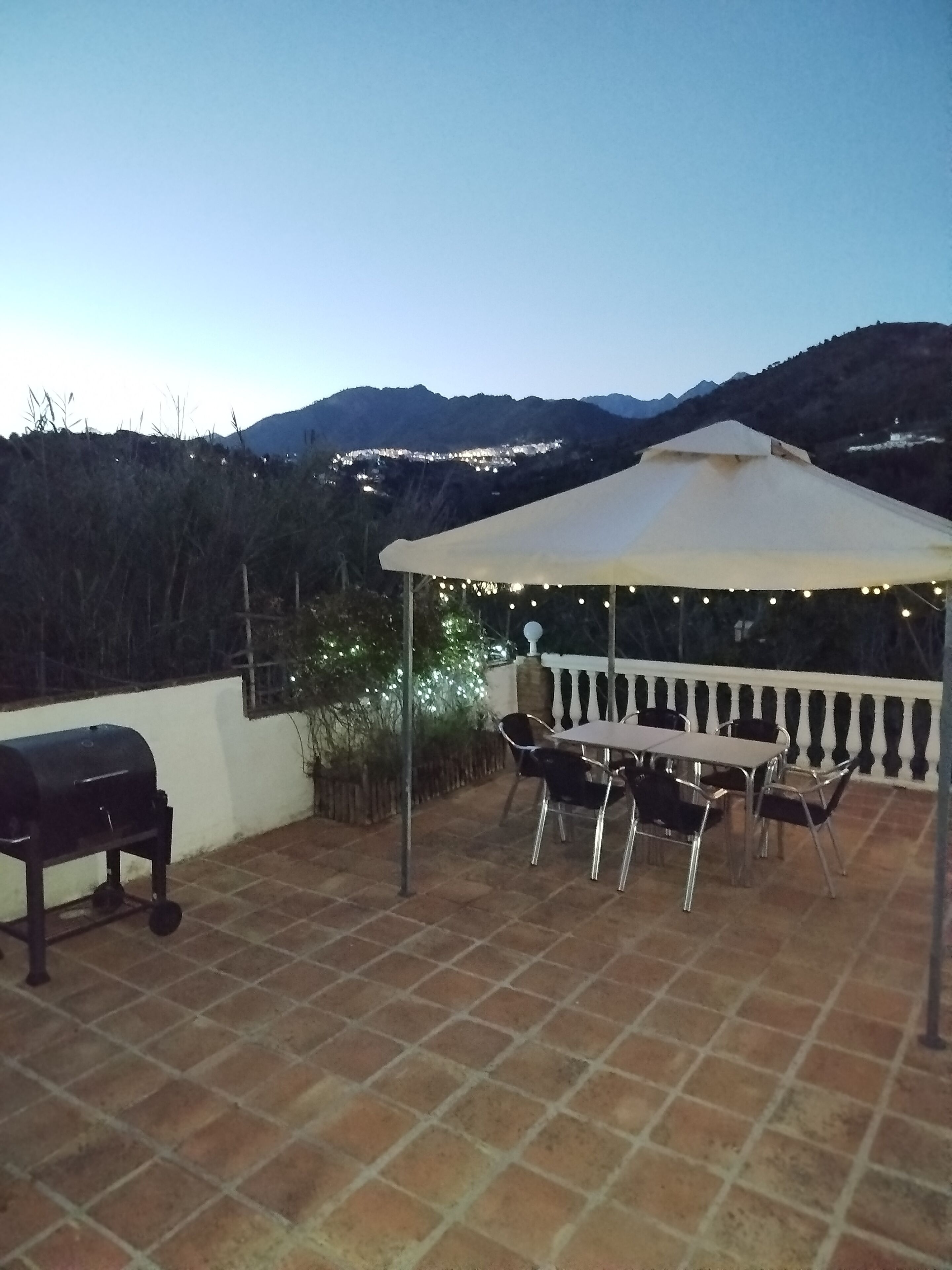 A patio with a barbecue grill, a table with chairs, and a canopy with string lights.