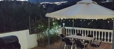 A patio with a barbecue grill, a table with chairs, and a canopy with string lights.