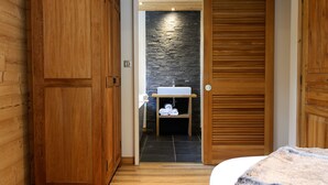 Une chambre avec des murs et un plafond en bois, un lit recouvert d’une couverture blanche et grise, une armoire en bois et un tapis blanc et moelleux sur le sol.