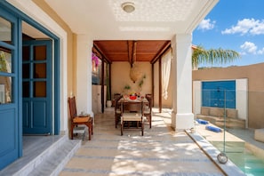 A sunlit patio with a dining table set for two, a pool area, and a blue door. - Villa Kallergi - Athena (640 m2) - north-western Crete with Concert Piano & Pool (Rethymnon)