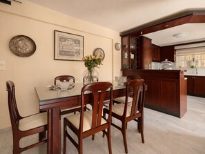 A dining area with a wooden table and chairs, a vase with flowers, and a kitchen area with wooden cabinets and a countertop.