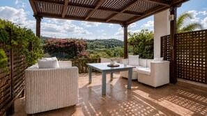 An outdoor patio with wicker furniture, a table, and a view of a hilly landscape. - Villa Kallergi - Athena (640 m2) - north-western Crete with Concert Piano & Pool (Rethymnon)