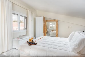 A bedroom with a large bed, a bedside table with a basket and a glass of orange juice, and a window with curtains.