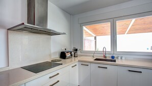 Een moderne keuken met witte kasten, een roestvrijstalen afzuigkap, een inbouwoven, een spoelbak en een raam met houten luiken.