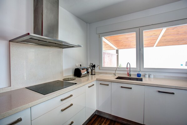 A modern kitchen with white cabinets, a stainless steel range hood, a built-in oven, a sink, and a window with wooden shutters. - New luxury villa, first line of the Mediterranean and the Mar Menor. (La Manga)