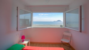 Een kamer met een bed, een stoel, een klein tafeltje en een raam met uitzicht op zee.