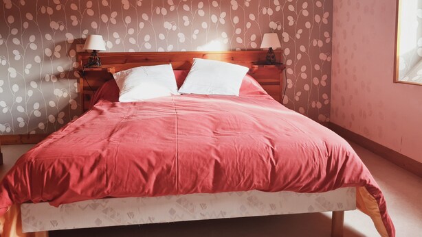 Un dormitorio con cabecera de madera, dos lámparas de noche, una colcha roja y un papel tapiz estampado.