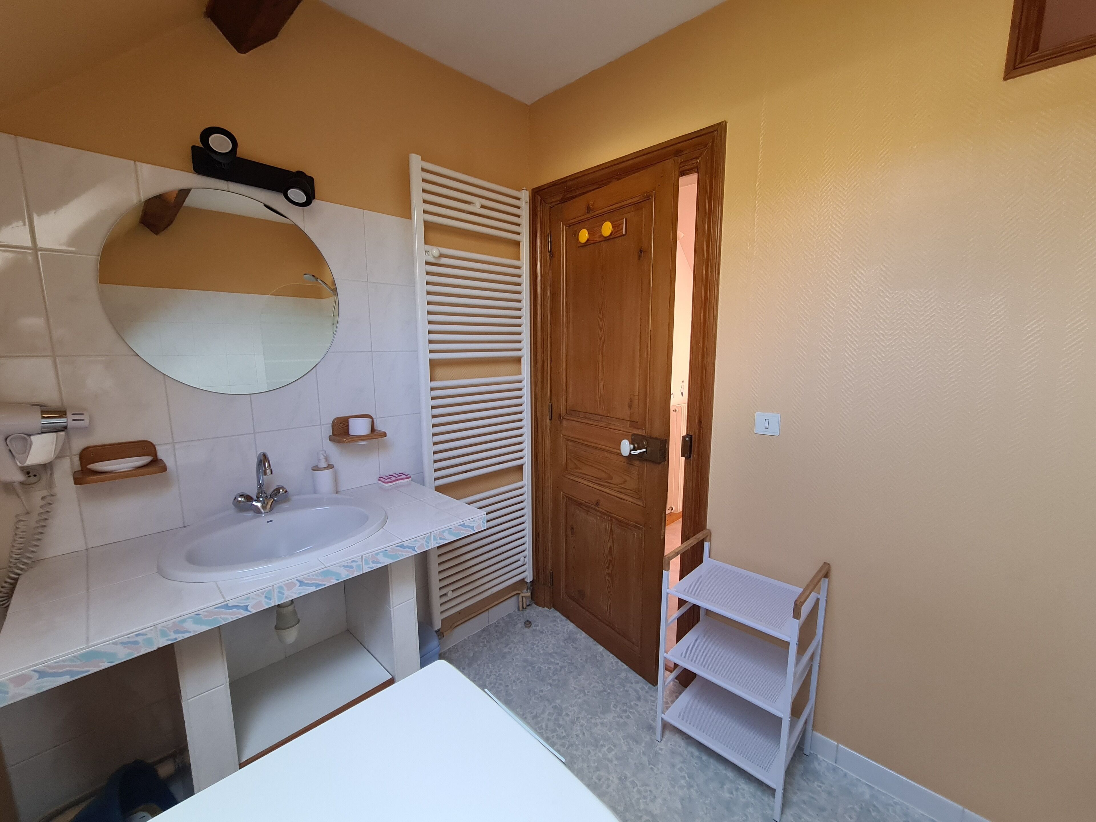 A bathroom with a sink, mirror, towel rack, and a wooden door.