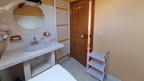 Un baño con lavabo, espejo, perchero para toallas y una puerta de madera.