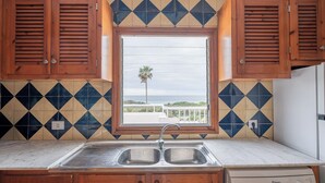 Una cocina con un lavamanos doble, armarios de madera, un lavavajillas Balay y una ventana con vista al océano.