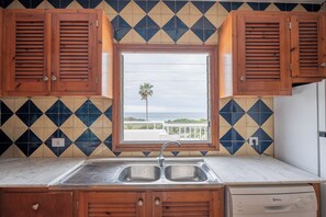 A kitchen with a double sink, wooden cabinets, a Balay dishwasher, and a window with a view of the ocean.