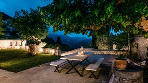 An outdoor patio with a stone table and benches, surrounded by greenery and stone walls. - Siora Tanto Villa, a combination of rustic charm and modern flair!  (Lefkada)