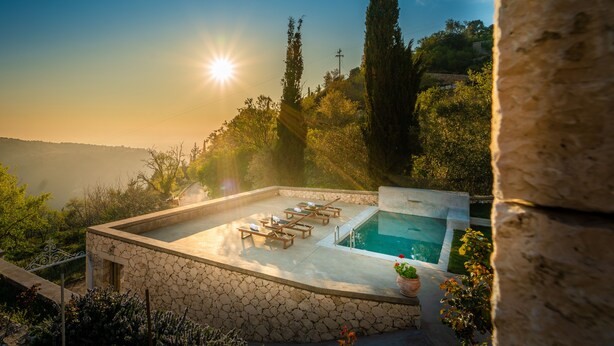 A pool area with lounge chairs and a hot tub, surrounded by stone walls and greenery, with a view of the landscape. - Siora Tanto Villa, a combination of rustic charm and modern flair!  (Lefkada)