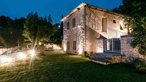 A stone building with a staircase leading to a balcony, surrounded by a well-maintained lawn and trees. - Siora Tanto Villa, a combination of rustic charm and modern flair!  (Lefkada)
