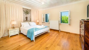 A bedroom with a bed, nightstands, a dresser, a window with a view, and a ceiling with wooden beams. - Siora Tanto Villa, a combination of rustic charm and modern flair!  (Lefkada)