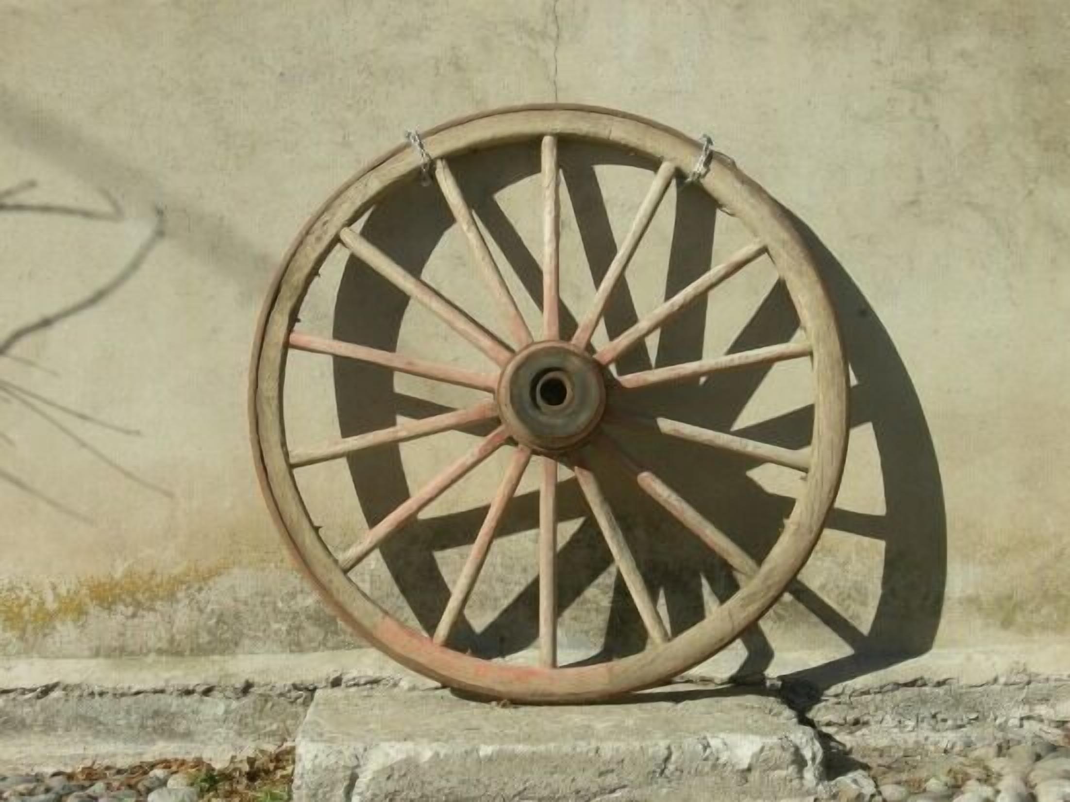 Una rueda de madera con radios, montada sobre una base de piedra frente a un muro liso.