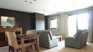 Een moderne woonkamer met een eetgedeelte, met een bank, fauteuils en een houten eettafel met stoelen.