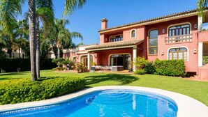 Une grande maison avec une piscine, entourée de pelouses bien entretenues et de palmiers.
