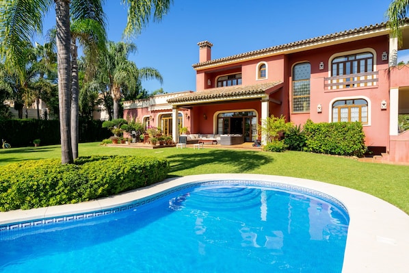Une grande maison avec une piscine, entourée de pelouses bien entretenues et de palmiers.