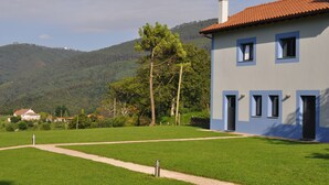 A two-story building with a red-tiled roof, a well-maintained lawn, and a mountainous backdrop. - Rural apartment Casona la Sierra for 4 people (Cudillero)