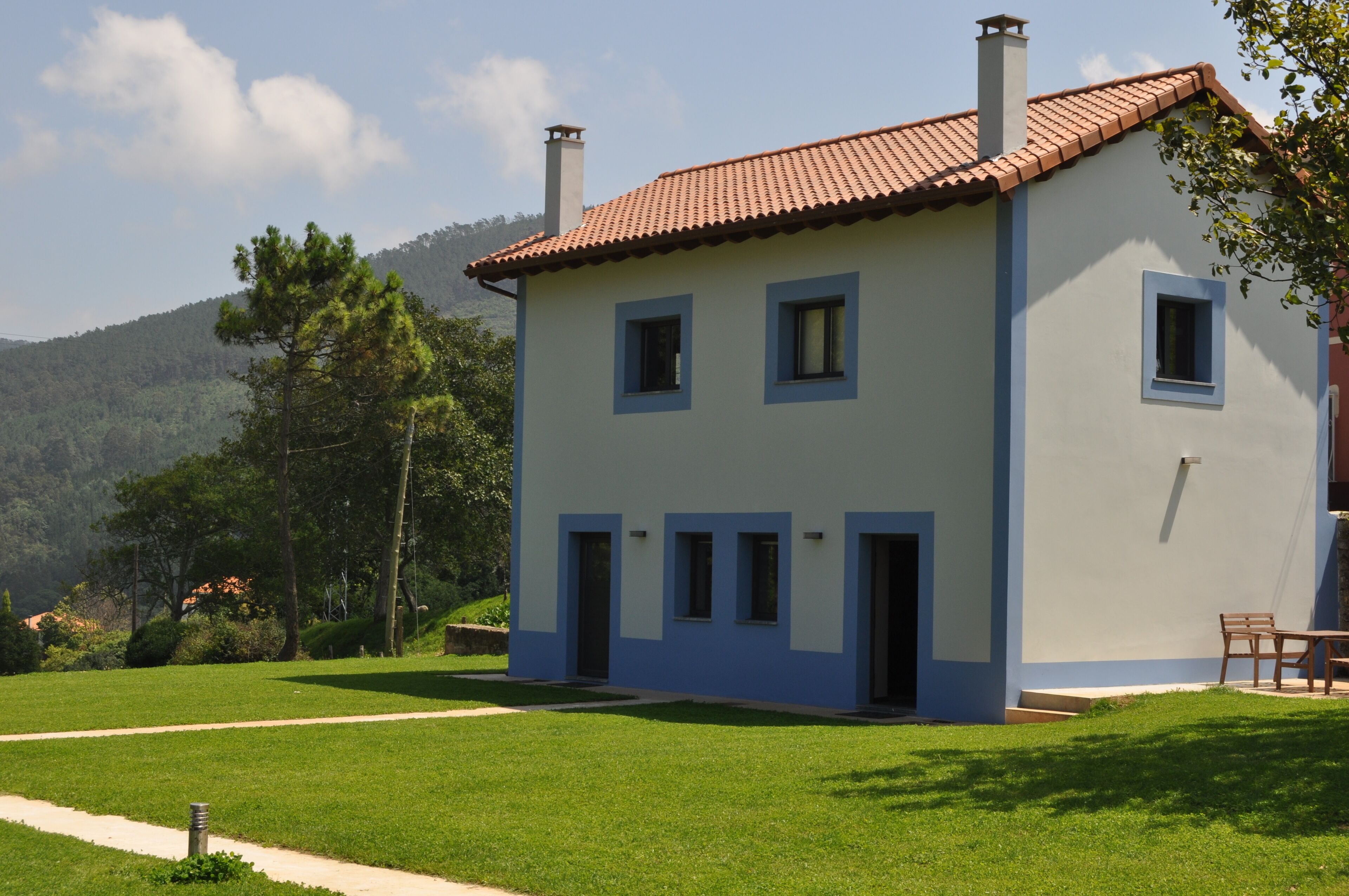 Ein zweistöckiges Haus mit rotem Ziegeldach, blauen Verzierungen und einer kleinen Veranda mit Tisch und Stühlen.