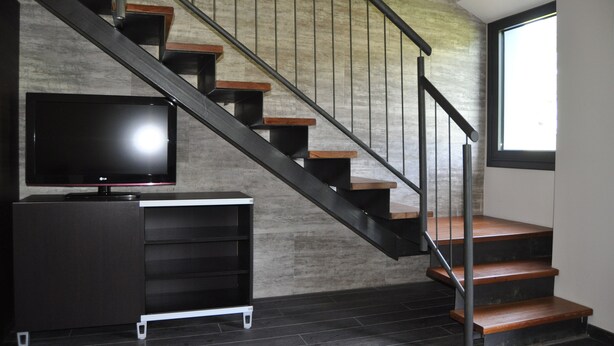 A staircase with wooden steps and metal railings, a flat-screen TV on a black cabinet, and a window with natural light. - Rural apartment Casona la Sierra for 4 people (Cudillero)