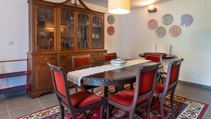 A dining area with a wooden cabinet, red upholstered chairs, a round table with a white tablecloth, and a patterned rug. - Casa do Loreto - Ponta Delgada (Fajã de Baixo)