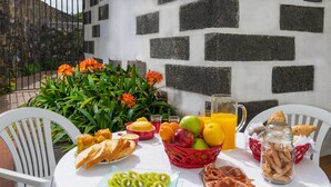 A table set with breakfast items including bread, fruit, and pastries, with a stone wall and plants in the background. - Casa do Loreto - Ponta Delgada (Fajã de Baixo)