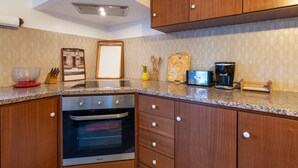 A kitchen with wooden cabinets, a built-in oven, a coffee maker, and a framed picture on the counter. - Casa do Loreto - Ponta Delgada (Fajã de Baixo)