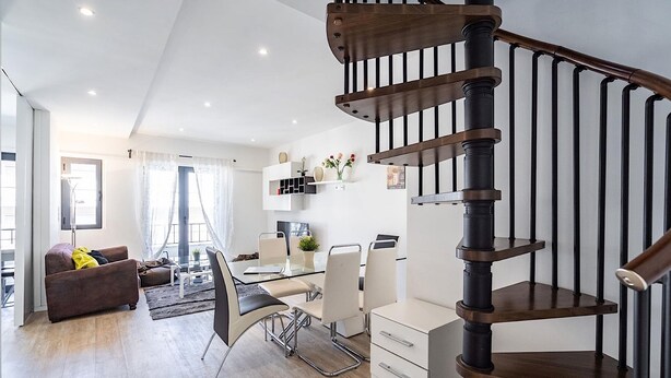 A modern living room with a staircase, a dining area, and a kitchen.